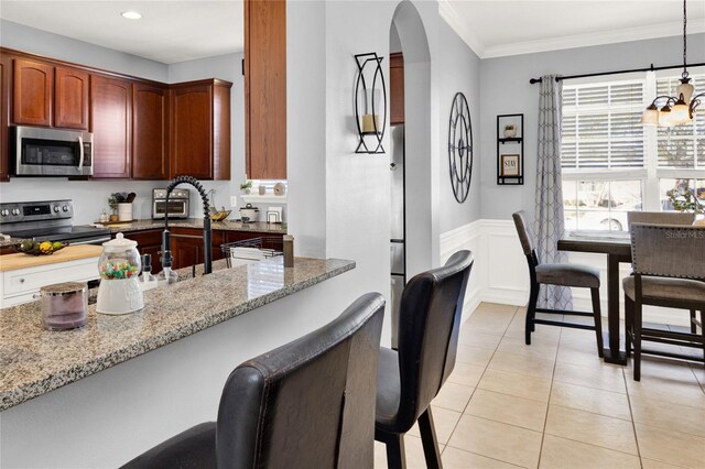 kitchen featuring arched walkways, a wainscoted wall, appliances with stainless steel finishes, light stone countertops, and a kitchen bar