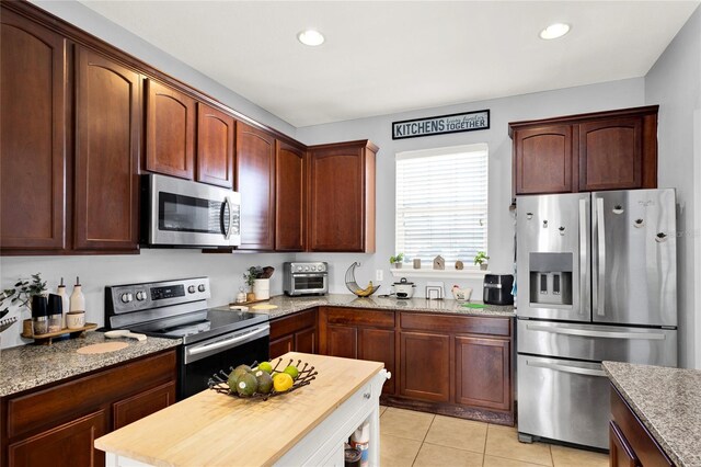 kitchen with light tile patterned floors, appliances with stainless steel finishes, light stone counters, and recessed lighting