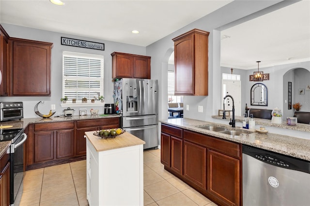 kitchen with light stone counters, arched walkways, light tile patterned floors, appliances with stainless steel finishes, and a sink