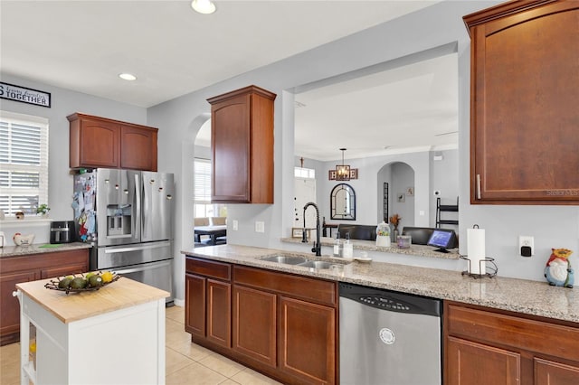 kitchen with light stone counters, arched walkways, light tile patterned floors, stainless steel appliances, and a sink