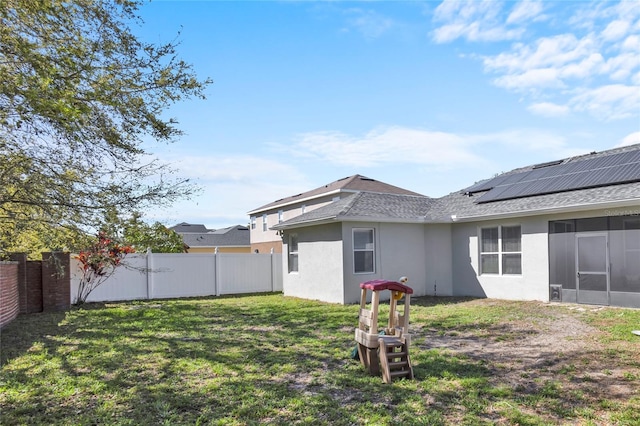 back of house featuring a fenced backyard, solar panels, a sunroom, a lawn, and stucco siding