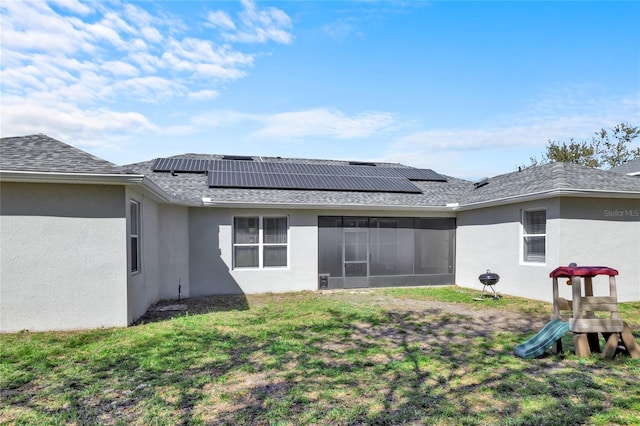 rear view of property featuring a playground, a yard, stucco siding, a sunroom, and roof mounted solar panels