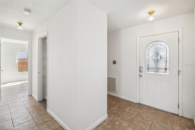 foyer entrance with a textured ceiling, light tile patterned floors, visible vents, and baseboards