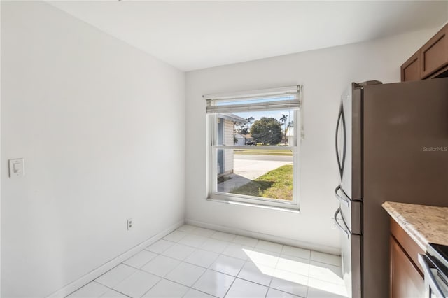 kitchen featuring baseboards, appliances with stainless steel finishes, brown cabinets, and light tile patterned flooring