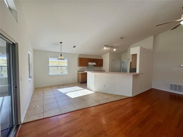 kitchen with lofted ceiling, ceiling fan, light wood-style flooring, visible vents, and brown cabinetry