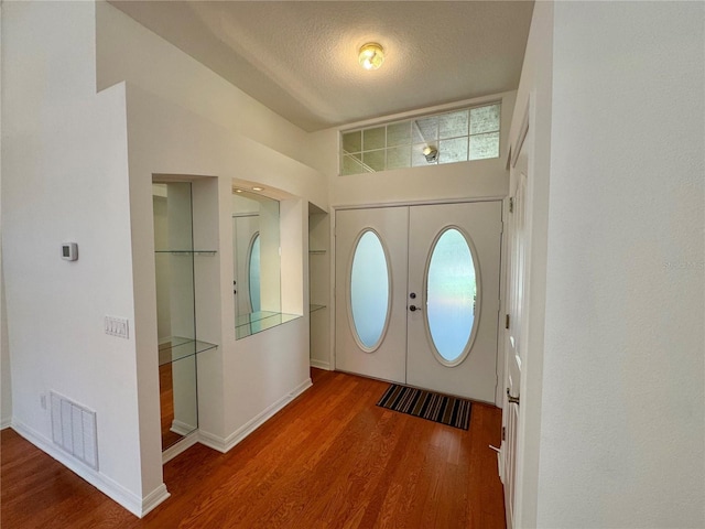 foyer with a textured ceiling, wood finished floors, visible vents, baseboards, and french doors