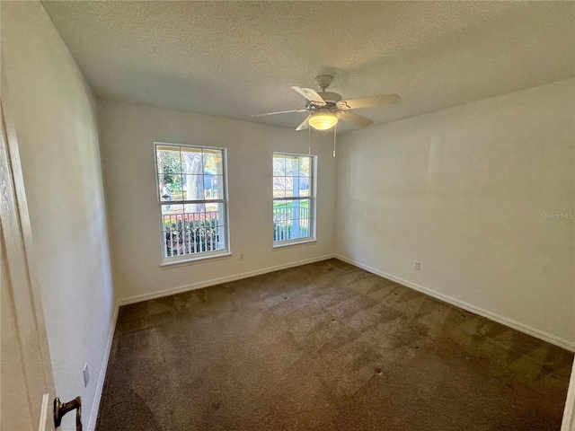 empty room with a textured ceiling, dark carpet, a ceiling fan, and baseboards