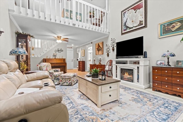 living room with stairway, a high ceiling, ornamental molding, a glass covered fireplace, and ceiling fan