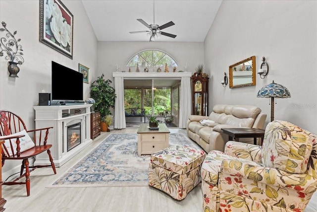 living area with light wood-type flooring, ceiling fan, lofted ceiling, and a glass covered fireplace