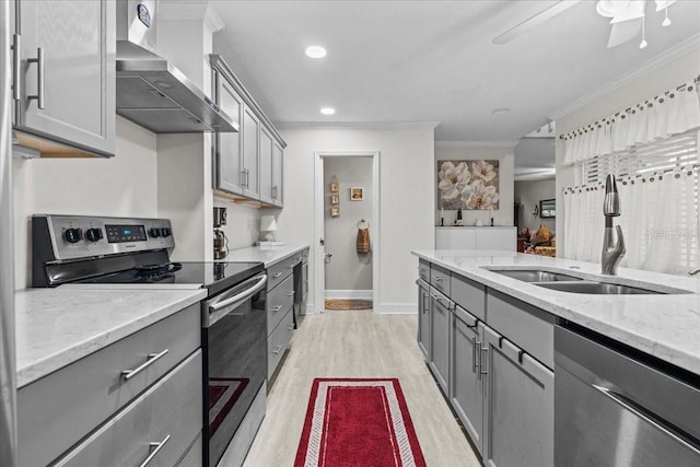 kitchen featuring appliances with stainless steel finishes, gray cabinets, a sink, and wall chimney range hood