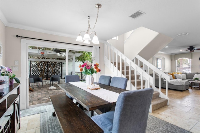 dining area featuring crown molding, ceiling fan with notable chandelier, stone tile flooring, visible vents, and stairs