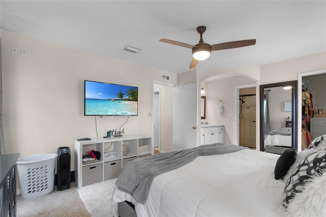 carpeted bedroom with connected bathroom, visible vents, arched walkways, and a ceiling fan