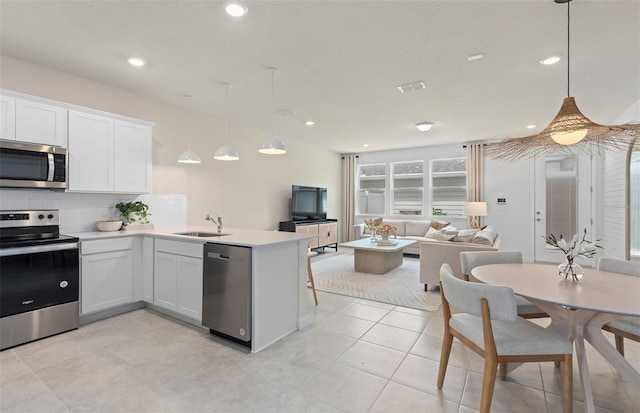 kitchen featuring white cabinets, decorative backsplash, appliances with stainless steel finishes, open floor plan, and a sink