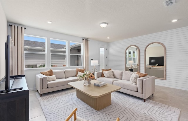 living room featuring light tile patterned floors, a textured ceiling, visible vents, and recessed lighting