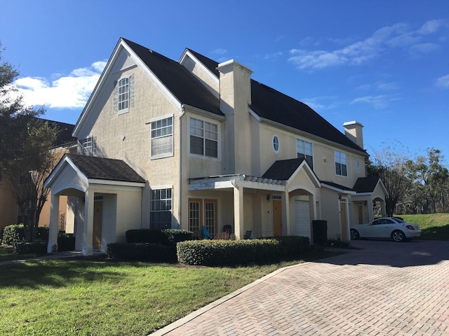 view of front of house featuring stucco siding, decorative driveway, a front yard, a garage, and a chimney