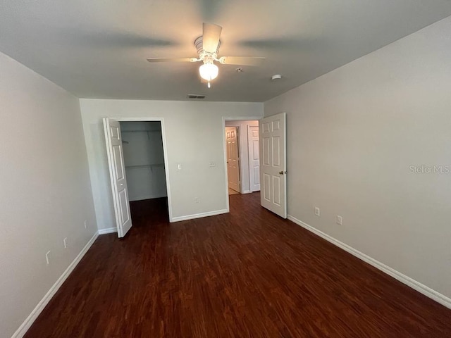 unfurnished bedroom with visible vents, a walk in closet, dark wood-type flooring, a ceiling fan, and baseboards