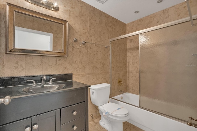 bathroom featuring tile walls, toilet, combined bath / shower with glass door, vanity, and tile patterned flooring