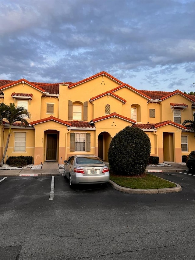 view of front facade with stucco siding, uncovered parking, and a tiled roof