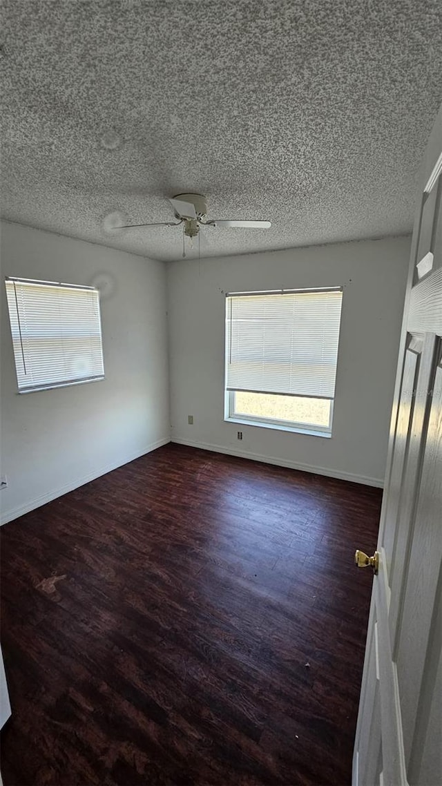 empty room featuring baseboards, a ceiling fan, dark wood finished floors, and a textured ceiling