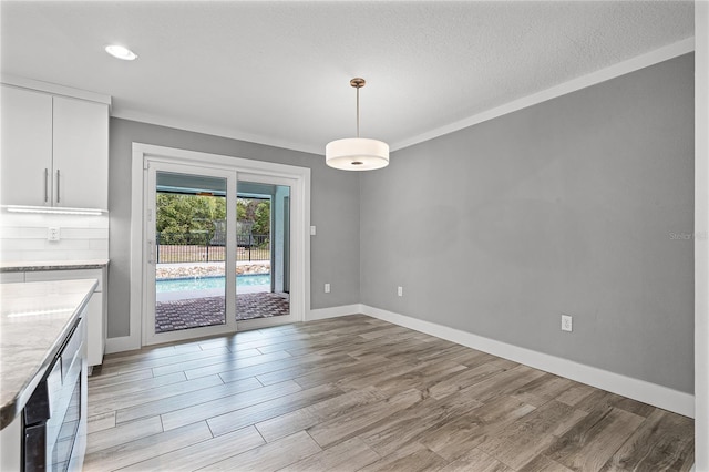 unfurnished dining area featuring baseboards, a textured ceiling, light wood-style flooring, and crown molding