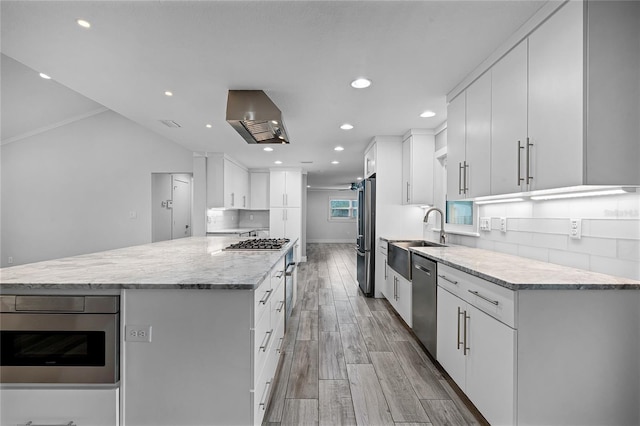 kitchen featuring backsplash, wall chimney range hood, light wood-type flooring, appliances with stainless steel finishes, and a sink