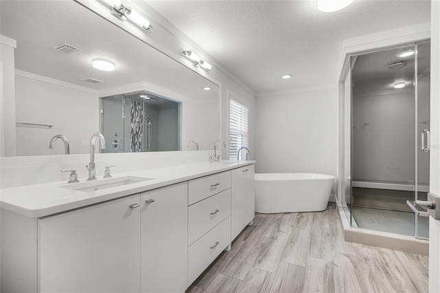 bathroom with wood finished floors, visible vents, double vanity, a freestanding tub, and a sink