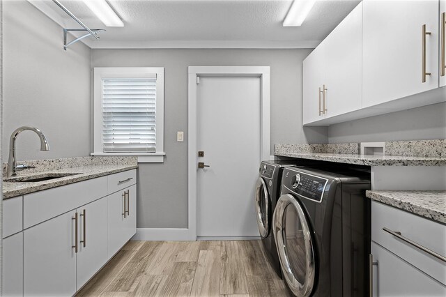 washroom with cabinet space, a sink, light wood-style floors, a textured ceiling, and washing machine and dryer