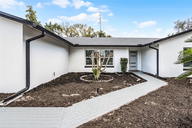 property entrance featuring stucco siding and a shingled roof