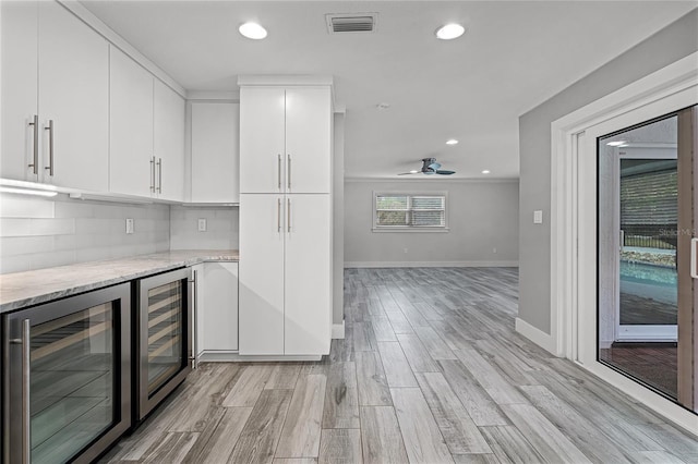 kitchen with light wood-type flooring, visible vents, beverage cooler, light stone counters, and white cabinetry