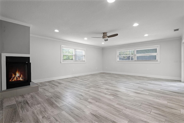 unfurnished living room featuring visible vents, a warm lit fireplace, crown molding, and light wood-style floors