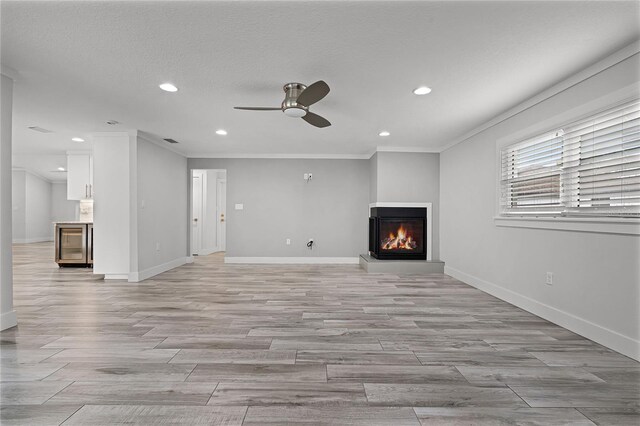 unfurnished living room featuring a glass covered fireplace, recessed lighting, light wood finished floors, baseboards, and ceiling fan