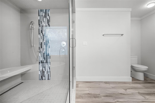 bathroom with a shower stall, toilet, baseboards, and wood finished floors