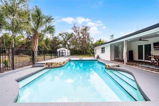 view of swimming pool with an outbuilding, a patio, fence, a storage shed, and ceiling fan