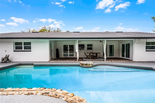 rear view of property with ceiling fan, an outdoor pool, and stucco siding