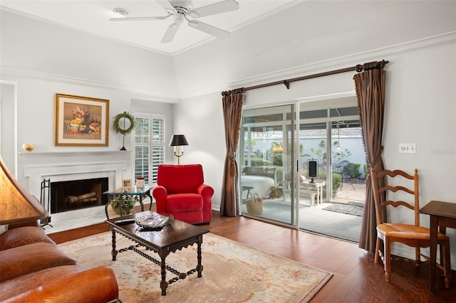 living room with a fireplace with flush hearth, wood finished floors, a ceiling fan, and crown molding