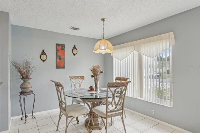 dining area with light tile patterned floors, visible vents, a textured ceiling, and baseboards