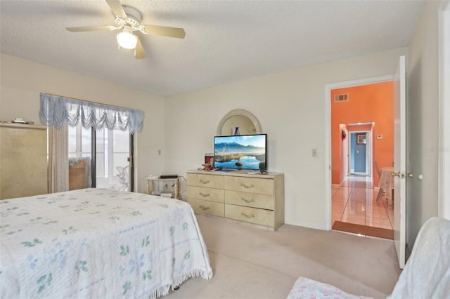 bedroom featuring visible vents, light carpet, a textured ceiling, and ceiling fan