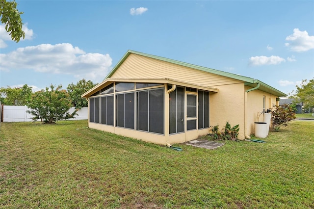 back of property with a yard, a sunroom, stucco siding, and fence