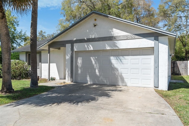 view of front of property featuring driveway, an attached garage, fence, and stucco siding