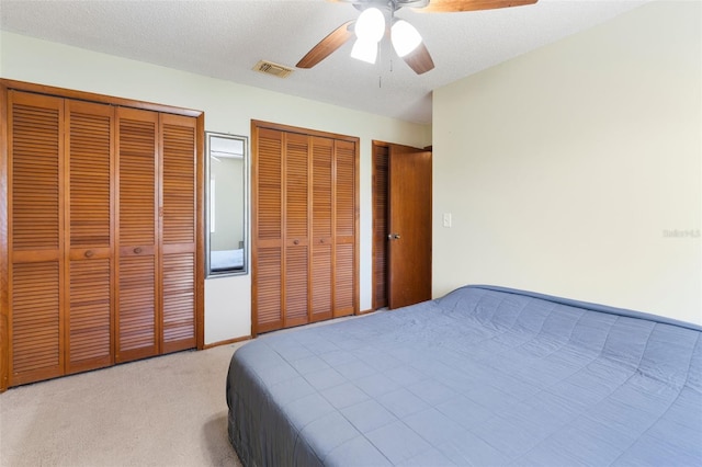 bedroom featuring visible vents, a ceiling fan, light colored carpet, a textured ceiling, and multiple closets