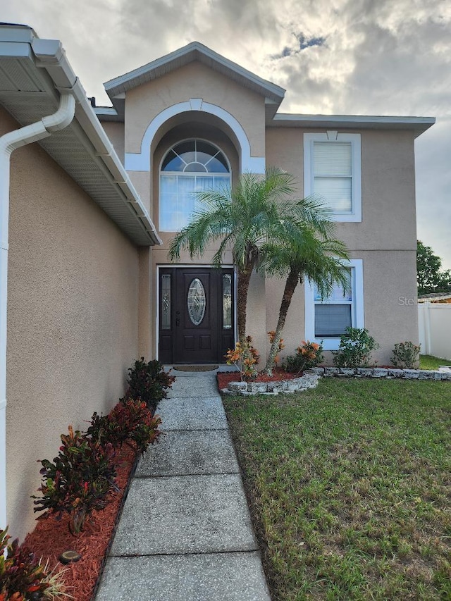 view of exterior entry with stucco siding and a yard