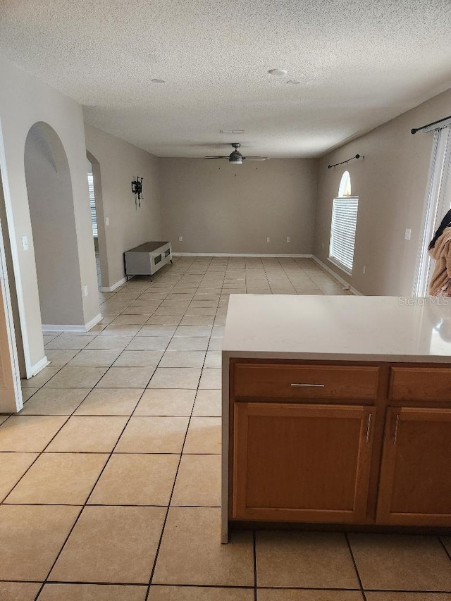 kitchen with light tile patterned floors, arched walkways, ceiling fan, and light countertops