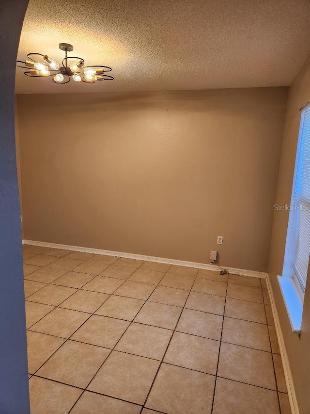 unfurnished room with baseboards, a textured ceiling, an inviting chandelier, and light tile patterned flooring