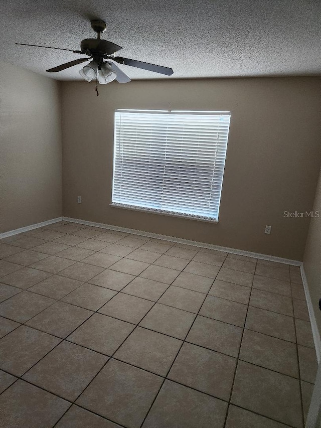 tiled empty room with baseboards, a textured ceiling, and ceiling fan