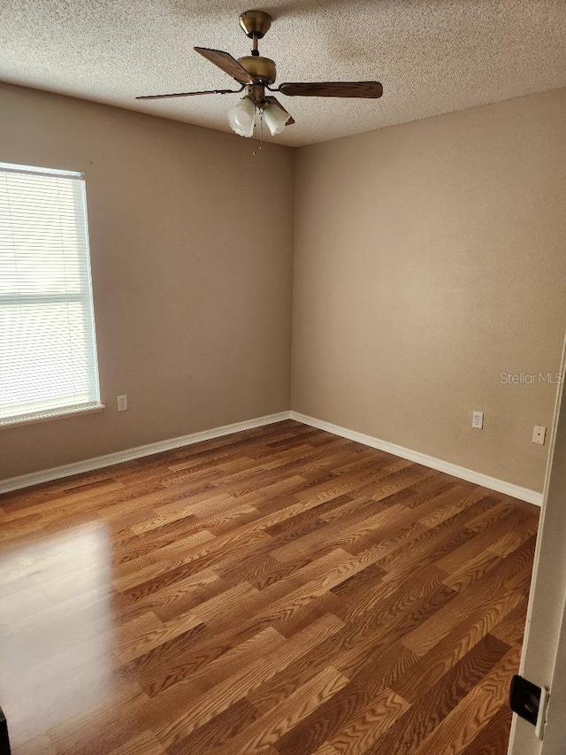 spare room with a ceiling fan, wood finished floors, baseboards, and a textured ceiling