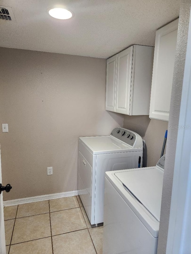 laundry area featuring baseboards, visible vents, light tile patterned flooring, cabinet space, and washer and clothes dryer