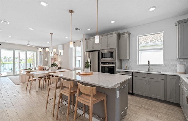 kitchen with tasteful backsplash, appliances with stainless steel finishes, a center island, gray cabinets, and a sink