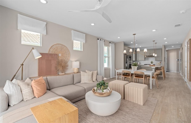 living area with recessed lighting, visible vents, light wood-style flooring, baseboards, and ceiling fan with notable chandelier