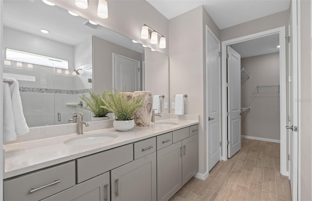 bathroom featuring double vanity, visible vents, wood finished floors, a shower stall, and a sink