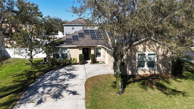 view of front of house featuring a front lawn, concrete driveway, roof mounted solar panels, and roof with shingles